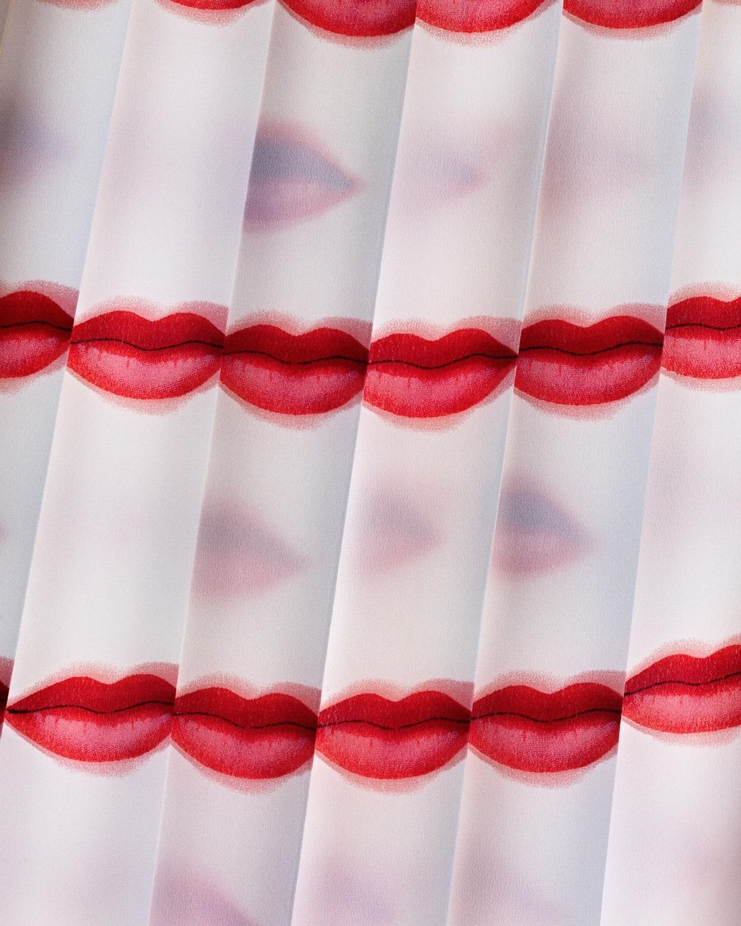 Close-up of a repeating pattern featuring illustrated red lips on a translucent, vertically pleated white fabric background.