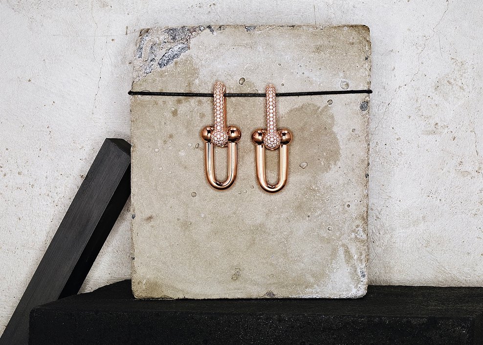 Studio shot of a pair of rose-gold-tone earrings with diamond accents displayed on a concrete surface with a dark background.