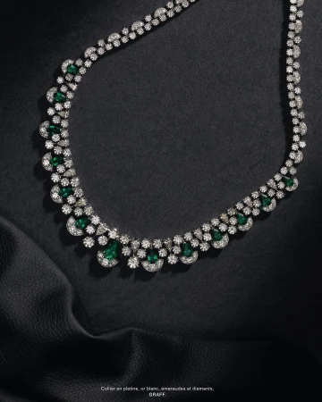 Elegant necklace featuring emeralds and diamonds against a draped black fabric background, showcased in a studio jewelry product shot.