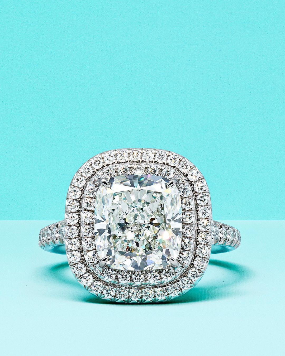 Close-up studio shot of a diamond ring with double halo setting on a light blue background. Jewelry for fashion and engagement concepts.