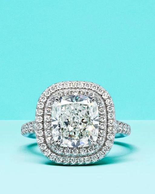 Close-up studio shot of a diamond ring with double halo setting on a light blue background. Jewelry for fashion and engagement concepts.