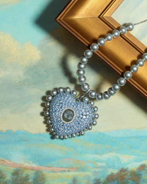 Heart-shaped necklace with pearl beads on an ornate gold frame against a painted landscape background. Jewelry fashion still life.