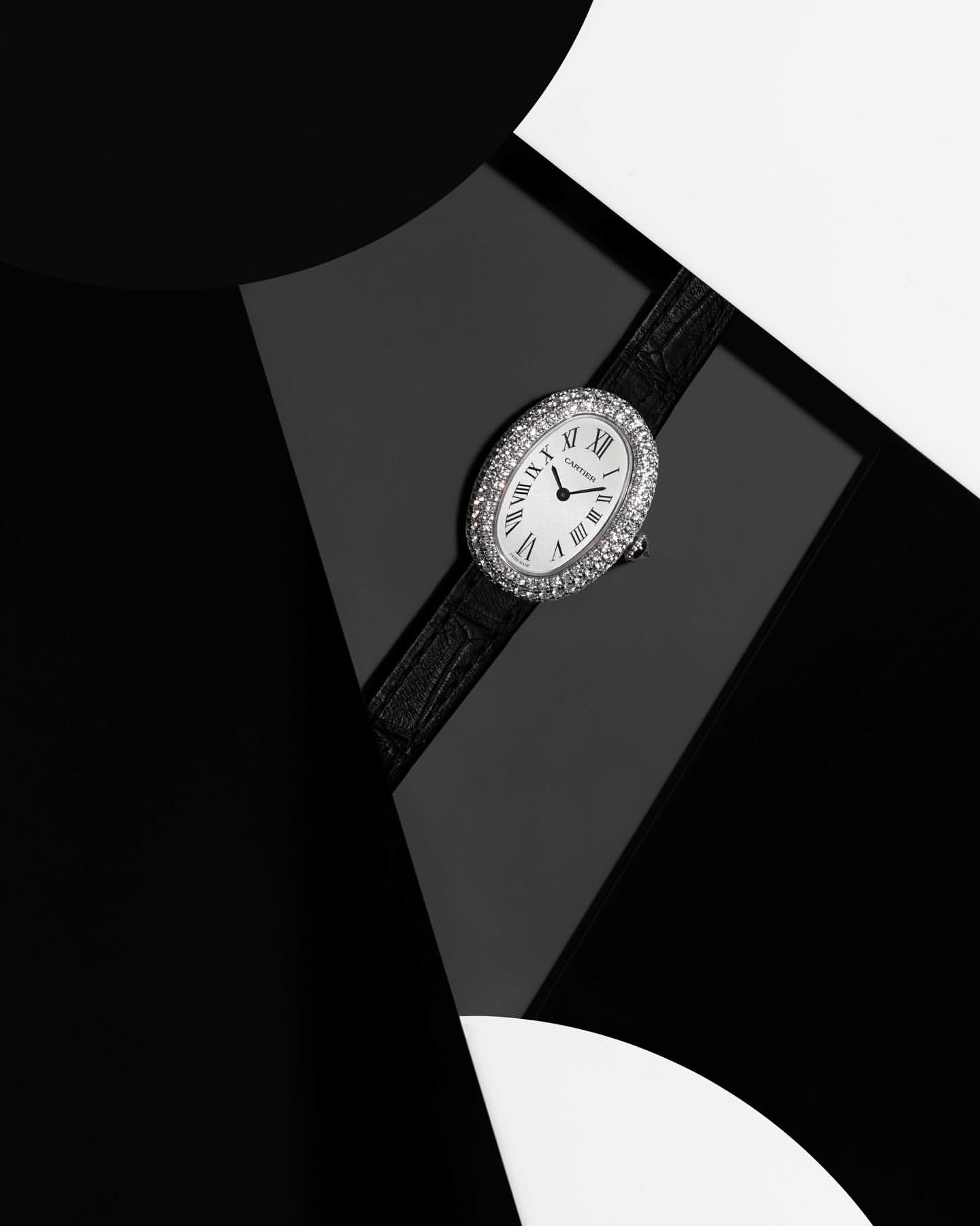 Close-up of an oval, diamond-encrusted wristwatch on a black leather strap, set against a geometric black and white background.