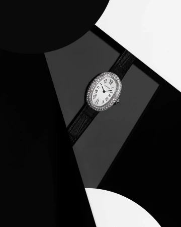 Close-up of an oval, diamond-encrusted wristwatch on a black leather strap, set against a geometric black and white background.