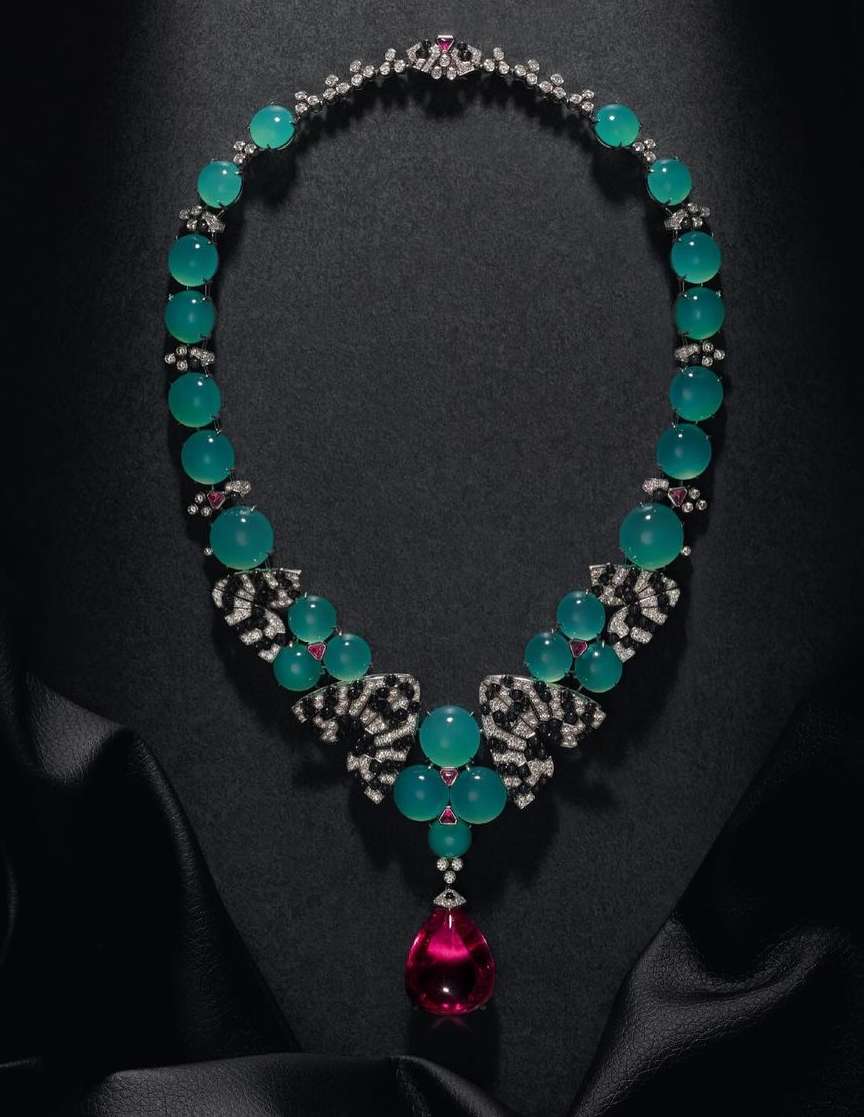 Elegant jewelry necklace on black satin, featuring teal beads, clear and black gem accents, and a large pink teardrop pendant.