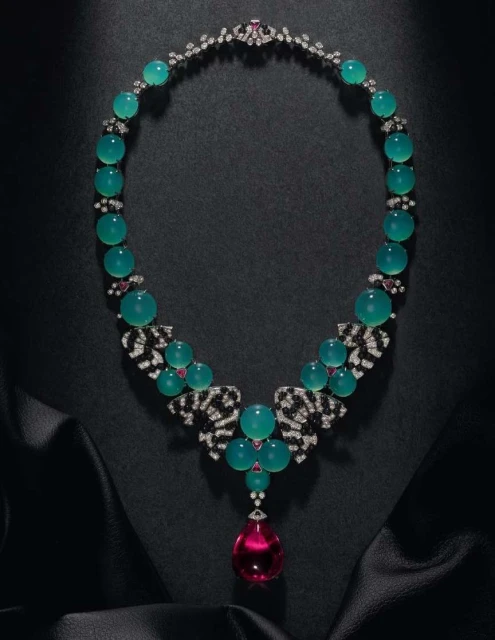 Elegant jewelry necklace on black satin, featuring teal beads, clear and black gem accents, and a large pink teardrop pendant.