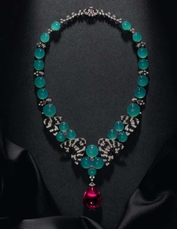 Elegant jewelry necklace on black satin, featuring teal beads, clear and black gem accents, and a large pink teardrop pendant.