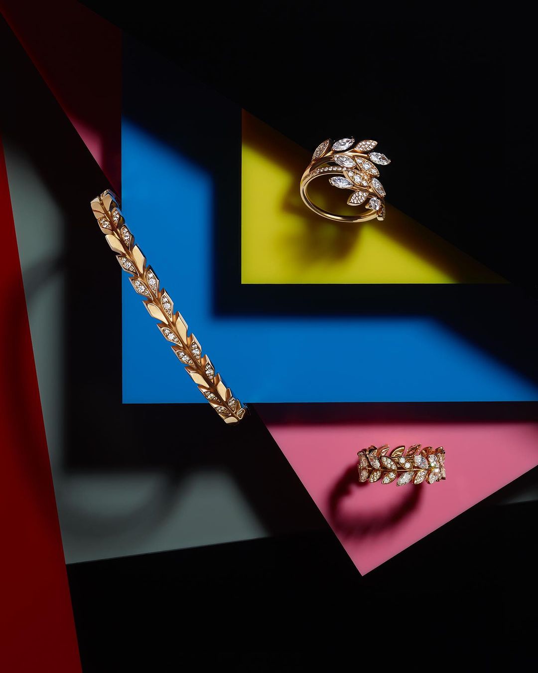 Still life close-up of golden fine jewelry on contrasting geometric colored papers: ring and bracelet form a striking composition.
