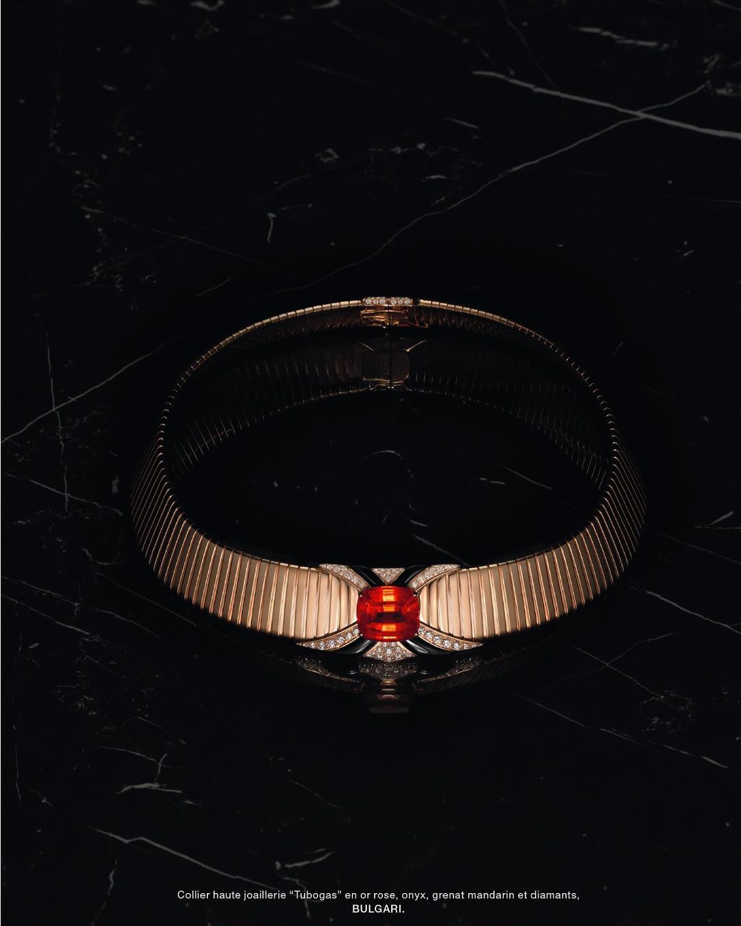 Elegant gold Bulgari 'Tubogas' necklace with mandarin garnet and diamonds showcased on a black marble surface, luxury jewellery still life.