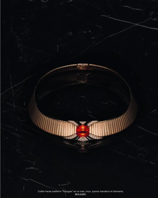 Elegant gold Bulgari 'Tubogas' necklace with mandarin garnet and diamonds showcased on a black marble surface, luxury jewellery still life.