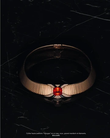 Elegant gold Bulgari 'Tubogas' necklace with mandarin garnet and diamonds showcased on a black marble surface, luxury jewellery still life.
