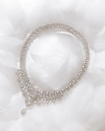Elegant diamond necklace on a bed of white feathers, showcasing its intricate design and luxurious sparkle against a soft, airy backdrop.