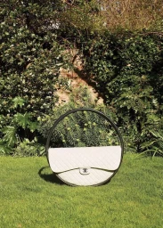 White quilted circular handbag resting on green grass in front of lush green foliage and brick wall