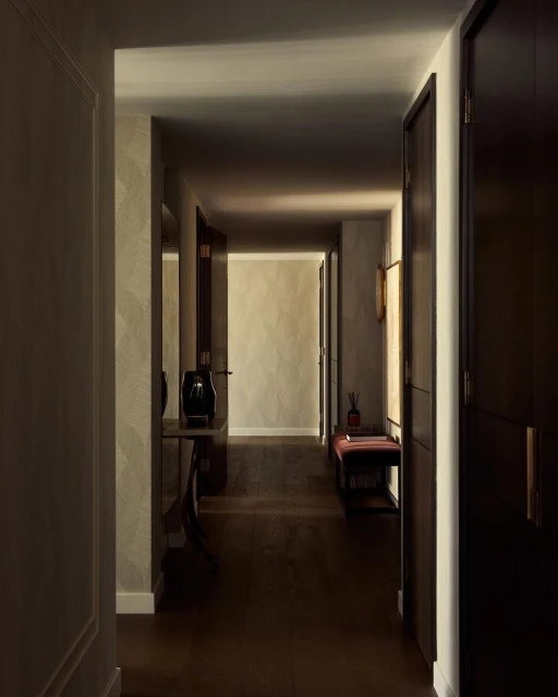 Interior hallway with hardwood floors, beige walls, dark wood doors, a table with decorative items, and bench seating by window.