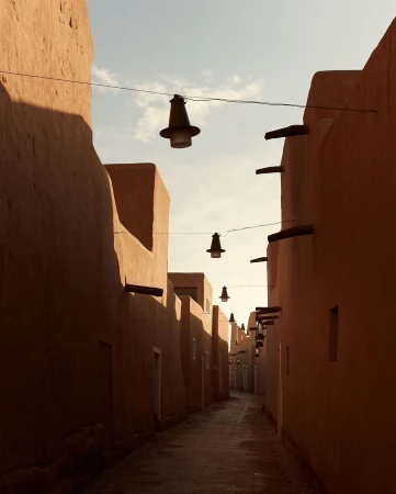 Narrow street lined with clay buildings and suspended lanterns, creating an atmospheric urban scene with soft lighting and architectural interest.