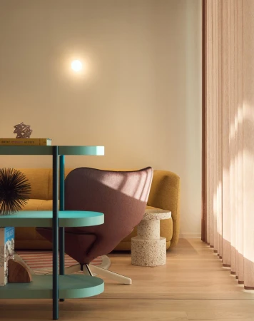 Interior design featuring a modern turquoise side table, purple lounge chair, speckled side table, and ochre couch in a sunlit room.