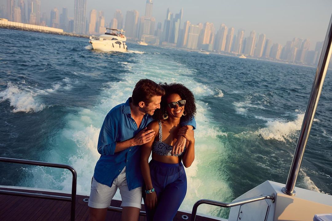 Couple enjoying a boat ride with Dubai's skyline in the background. A man embraces a woman on a boat with the city skyline visible.