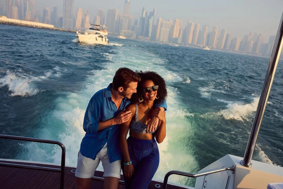 Couple enjoying a boat ride with Dubai's skyline in the background. A man embraces a woman on a boat with the city skyline visible.