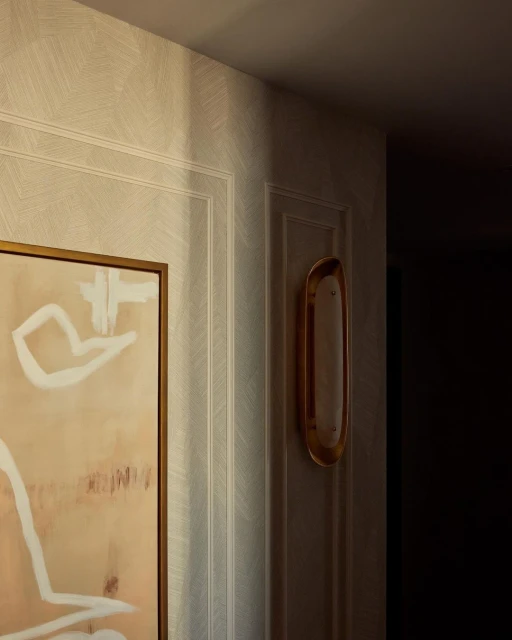 Interior design featuring an abstract painting with white and beige hues, complemented by a gold sconce on a textured wall.