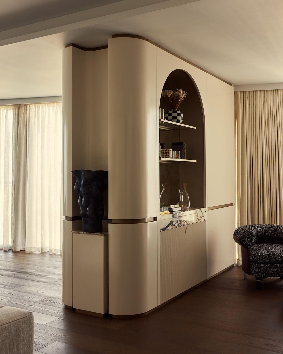Living room interior featuring a custom cream-colored shelving unit, hardwood floors, decorative objects, and soft, natural window light.