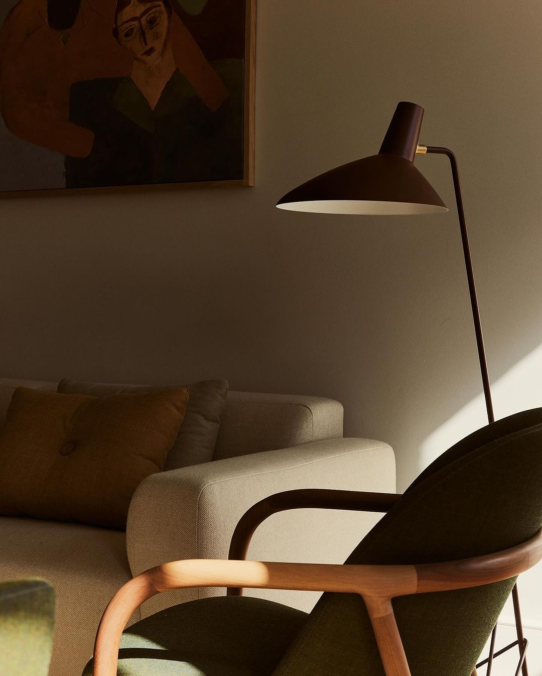 A warm-toned, inviting interior showcases a floor lamp illuminating a green chair, with a tan sofa and framed art in the background.