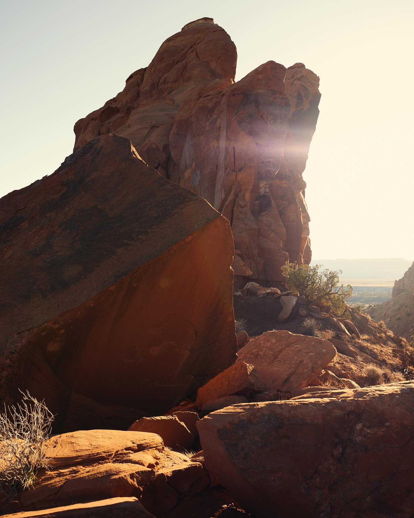 Dramatic view of a towering red rock formation against a clear sky, bathed in warm sunlight, in a natural outdoor setting.