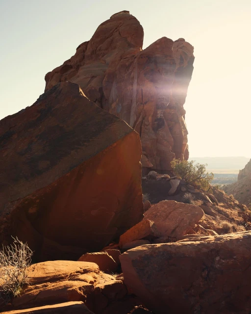 Dramatic view of a towering red rock formation against a clear sky, bathed in warm sunlight, in a natural outdoor setting. 