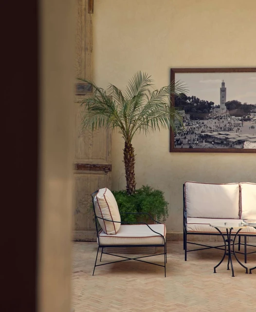 Outdoor lounge area featuring cushioned wrought iron chair and sofa, small round table, potted palm tree, and artwork in neutral tones.