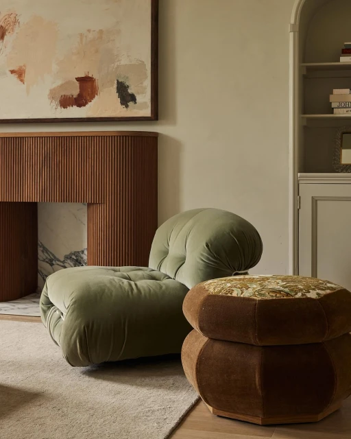 Interior with a light green velvet lounge chair and an ottoman, set on a neutral rug near a modern mantel and wall art.