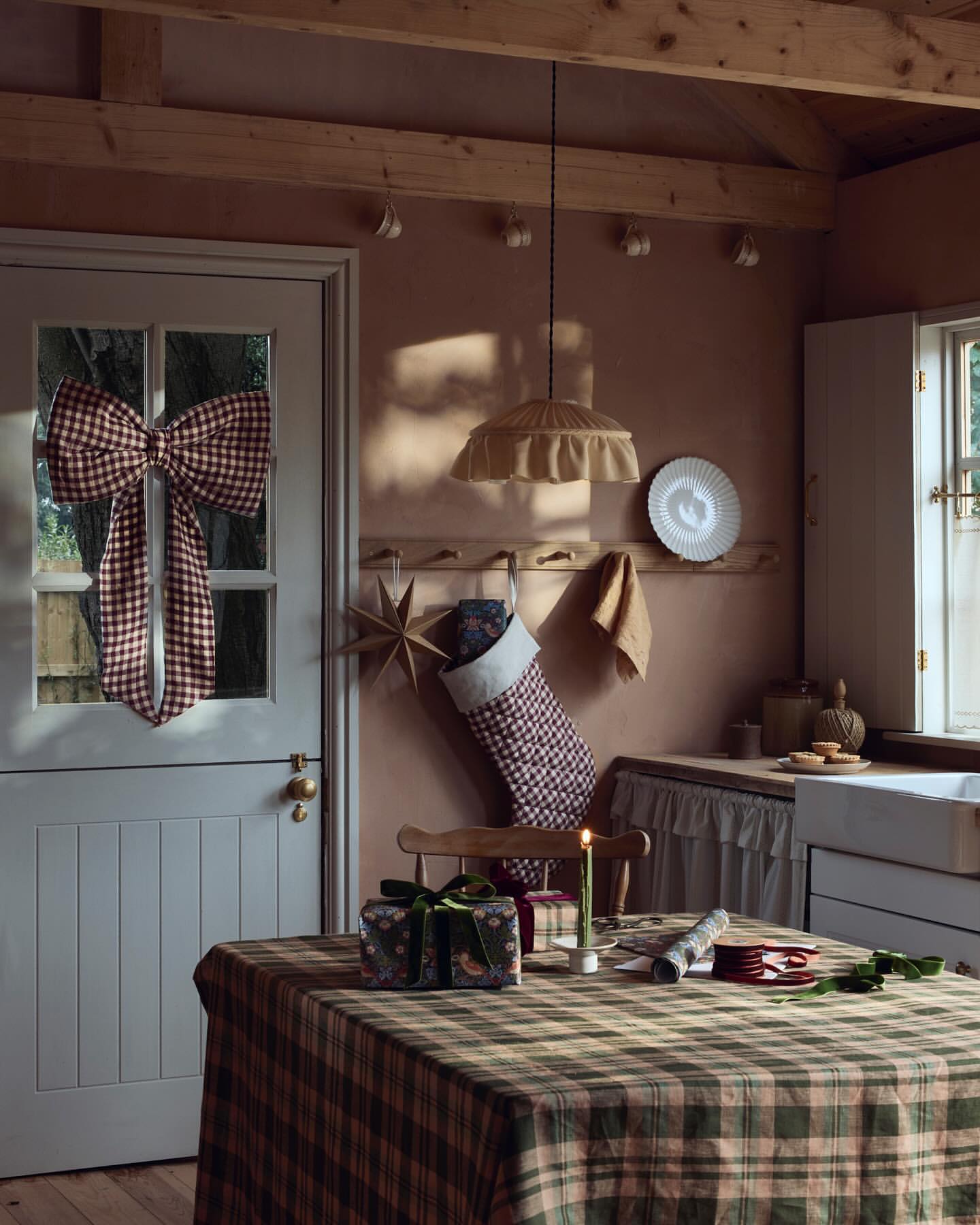 Festive interior with a plaid tablecloth, wrapped gift, and Christmas stocking, with a red-and-white bow adorning a door.