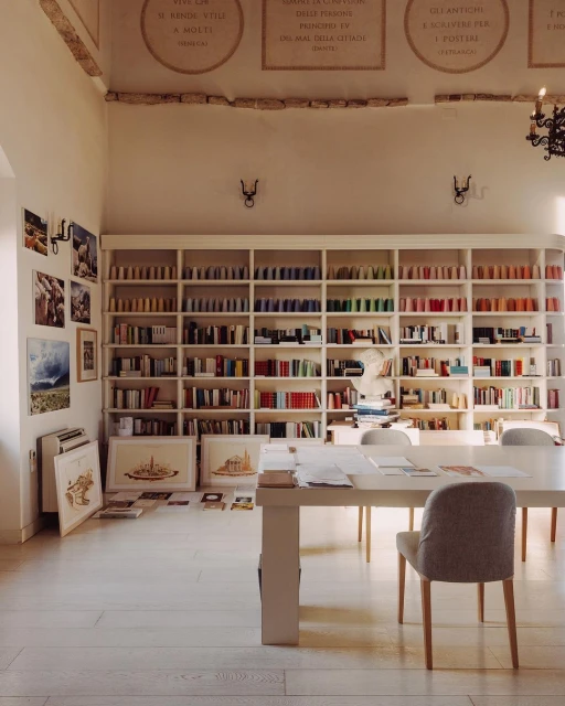 Brightly lit interior with large bookshelf filled with color-coded books, white tables, and art prints on the walls creates a serene ambiance.