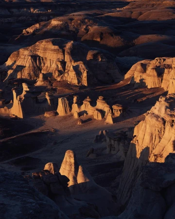 Dramatic golden light illuminates rock formations in a desert landscape. Eroded hoodoos and mesas create a stark, beautiful scene.