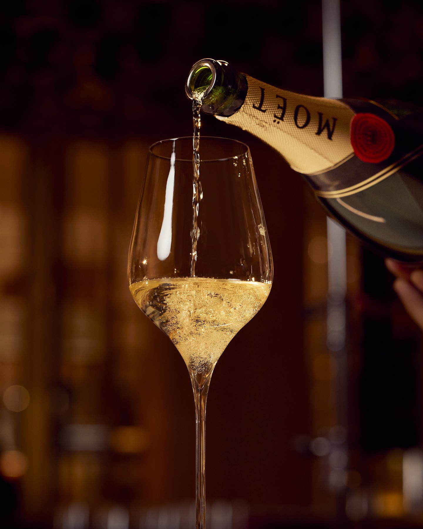 Close-up shot of champagne being poured into a stemmed glass, featuring a blurred background, indoor setting, and elegant ambiance.