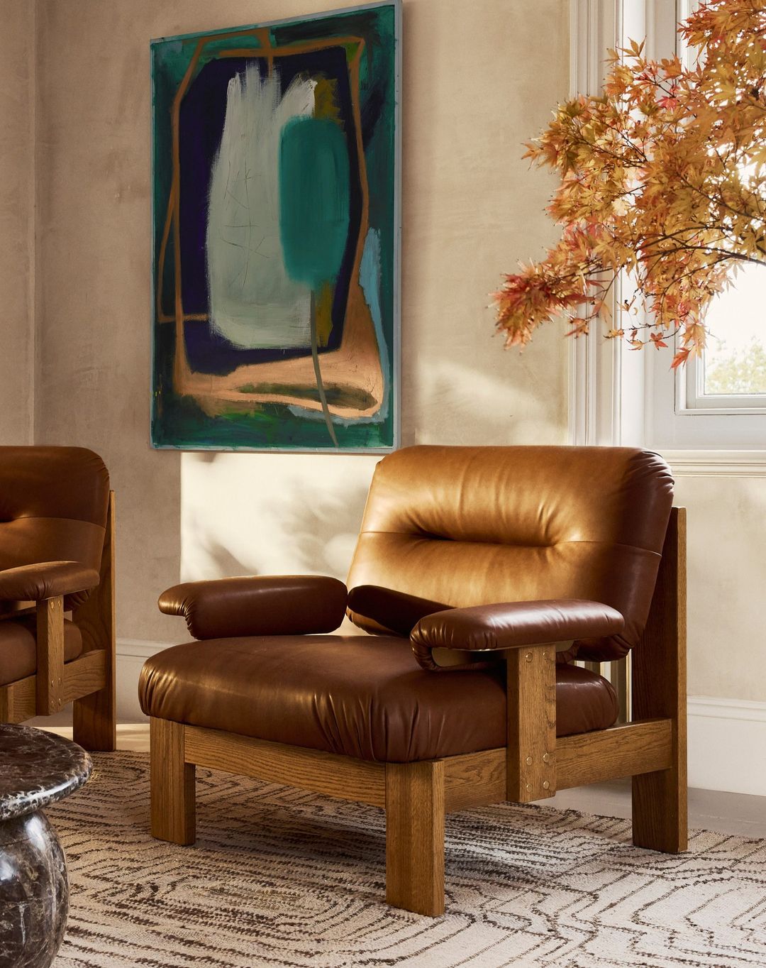 Living room interior featuring two brown leather armchairs, a patterned rug, and an abstract art piece on a beige wall.