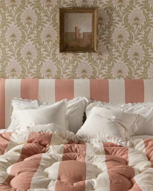 Bedroom interior with a striped duvet and headboard, white pillows, floral wallpaper, and framed art creates a cozy, inviting space.