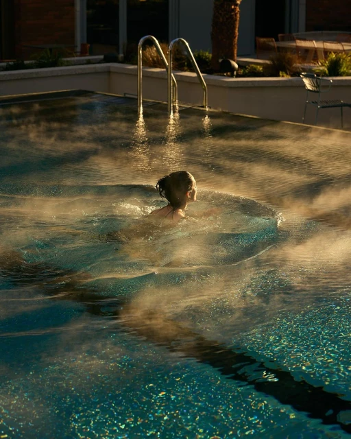 A child swims in an outdoor swimming pool with steam rising from the water, captured in golden light during late afternoon.