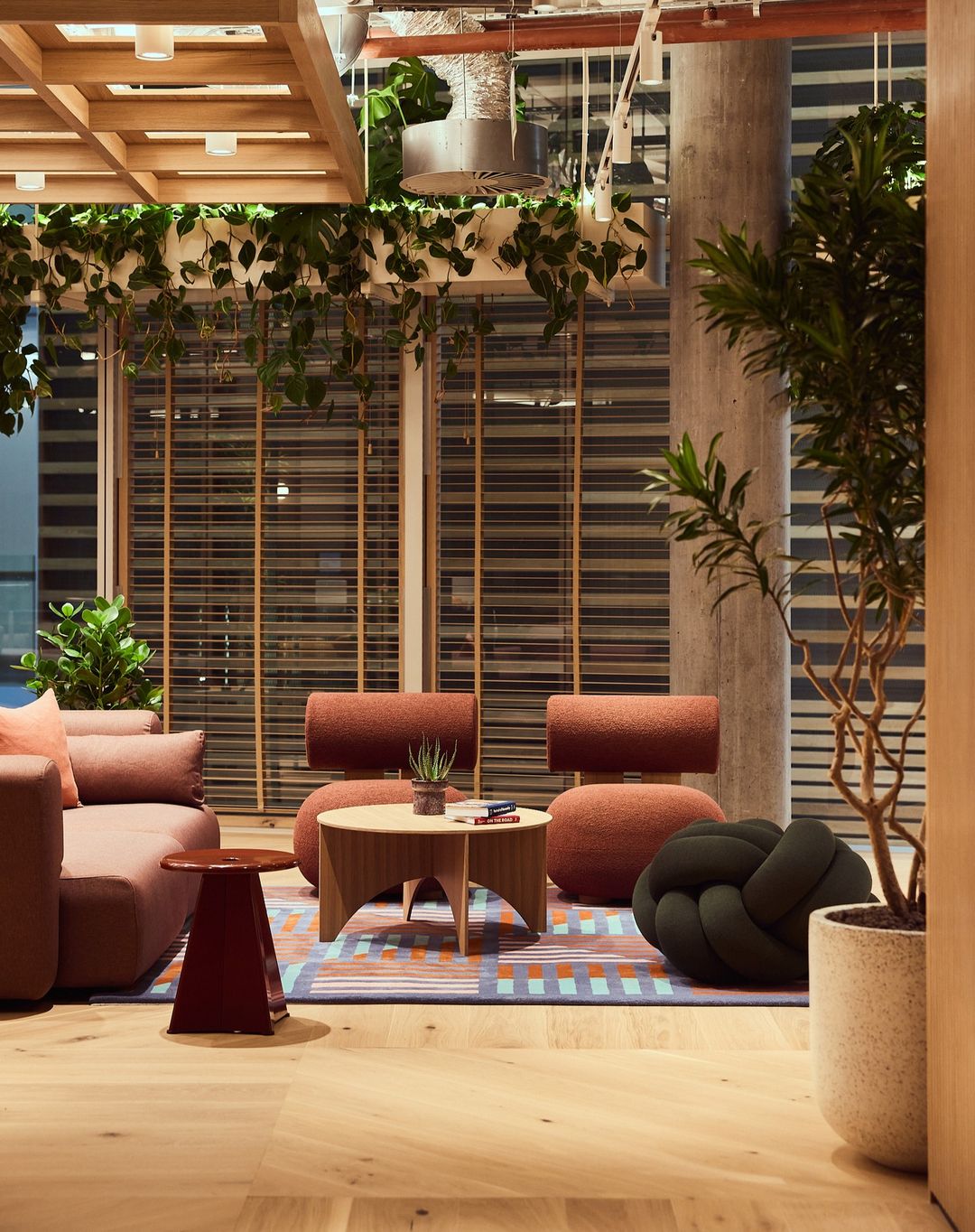 Modern office lounge area features neutral-toned furniture, decorative plants, natural light, and an inviting, collaborative space.