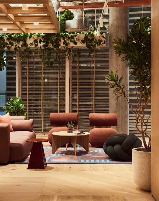 Modern office lounge area features neutral-toned furniture, decorative plants, natural light, and an inviting, collaborative space.