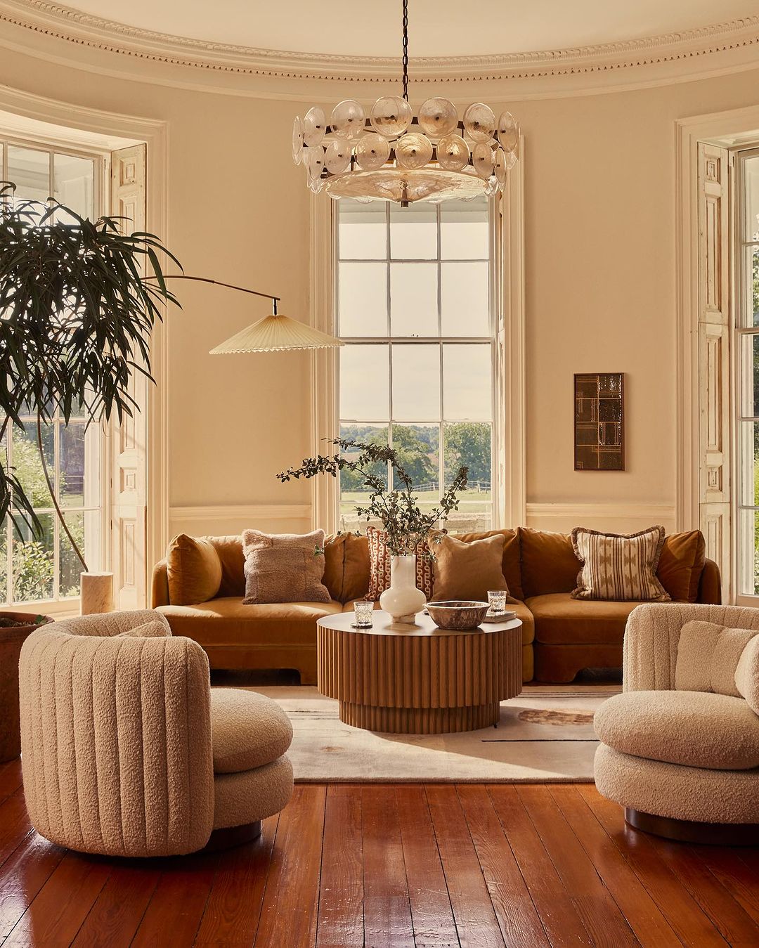 Living room interior featuring a brown sectional sofa, round coffee table, and modern chandelier in a well-lit, elegant space.