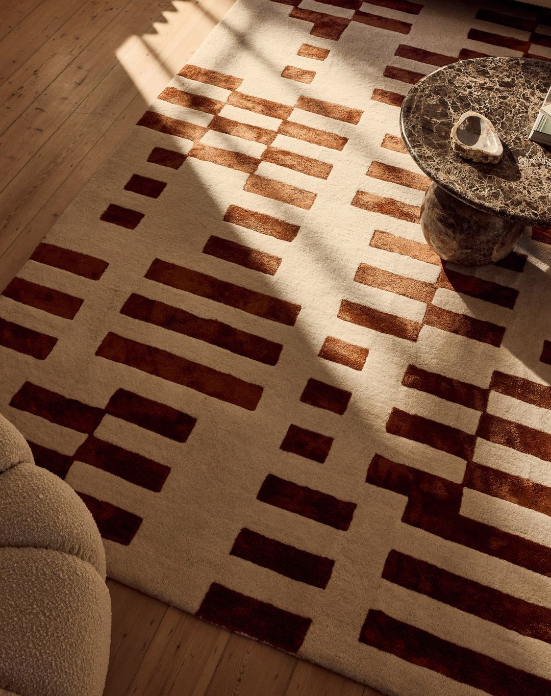 Interior shot of an area rug with a geometric pattern of rectangular shapes and a small round stone table and wooden floors.