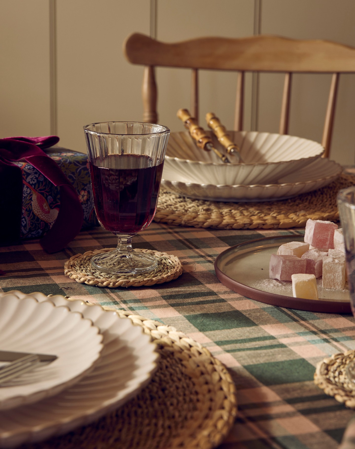 Still-life shot of a table setting with a wine glass, plates, Turkish delight, and a gift box under warm studio lighting.