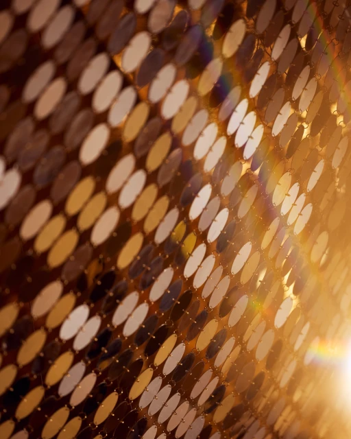 Abstract background of gold and silver metallic discs arranged in a pattern with a diagonal rainbow glare and bright light.