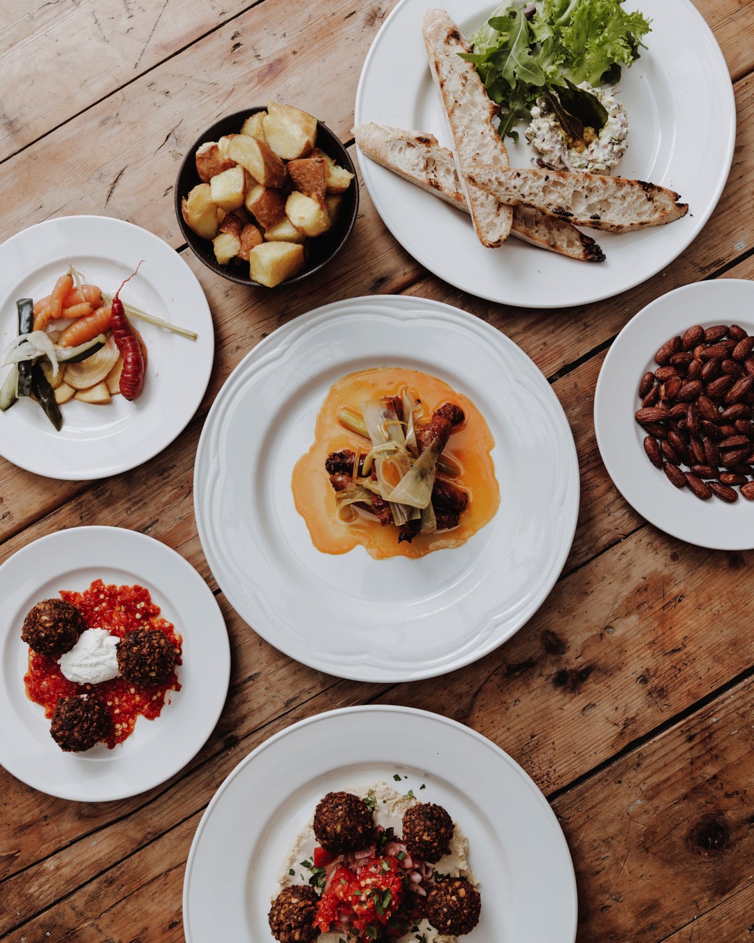 Overhead shot of a rustic wooden table featuring an assortment of colorful and diverse dishes arranged artfully on white plates.