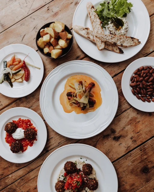 Overhead shot of a rustic wooden table featuring an assortment of colorful and diverse dishes arranged artfully on white plates.