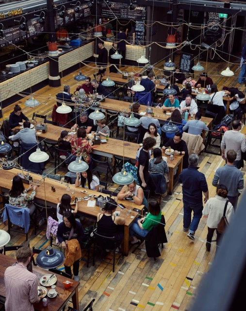 High-angle view of a bustling restaurant filled with people seated at wooden tables, illuminated by hanging pendant lights creating a warm ambiance.