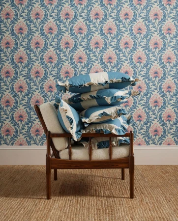 Interior scene with wooden chair stacked with striped blue and white ruffle pillows, floral patterned wallpaper, and jute rug.
