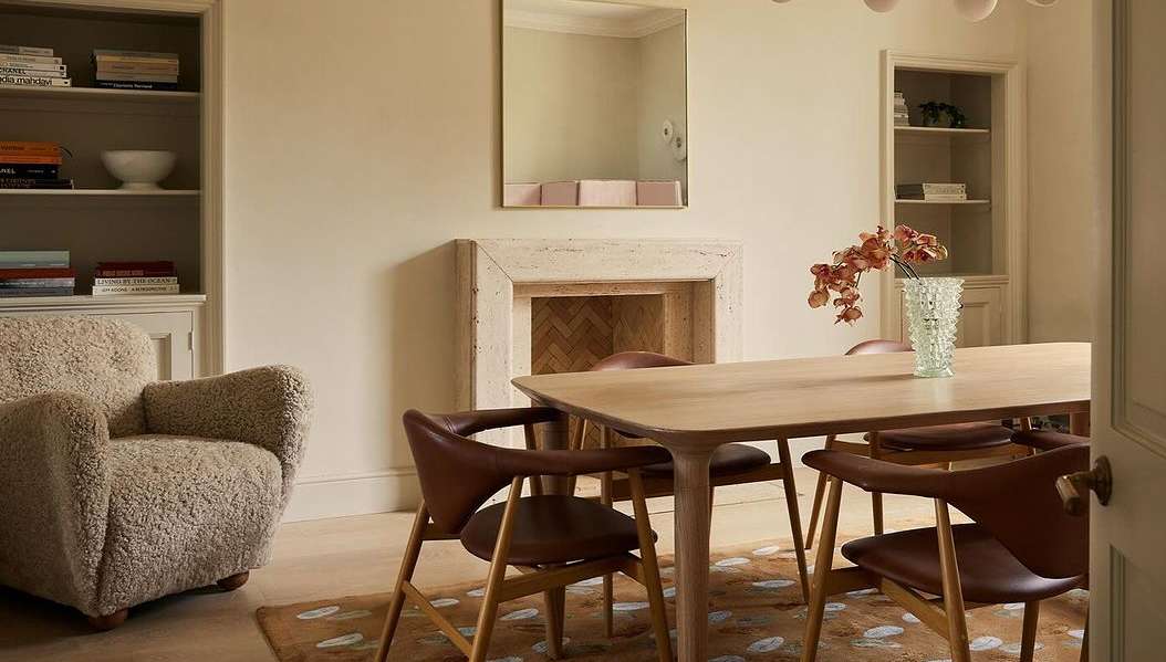 Indoor dining room featuring a light wood table surrounded by brown leather chairs, with a fireplace and beige walls and interior design.