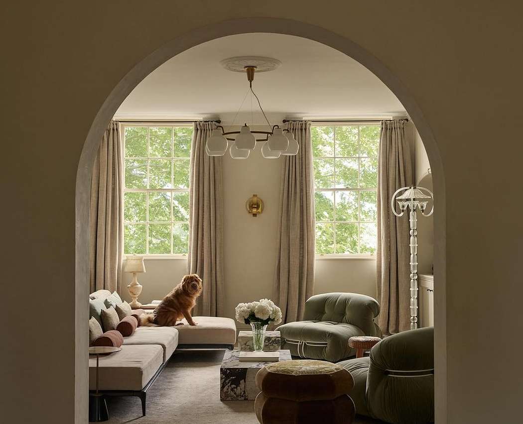 Interior view of a dog sitting on a sectional sofa in a living room with soft lighting, neutral color palette, and arched entryway.