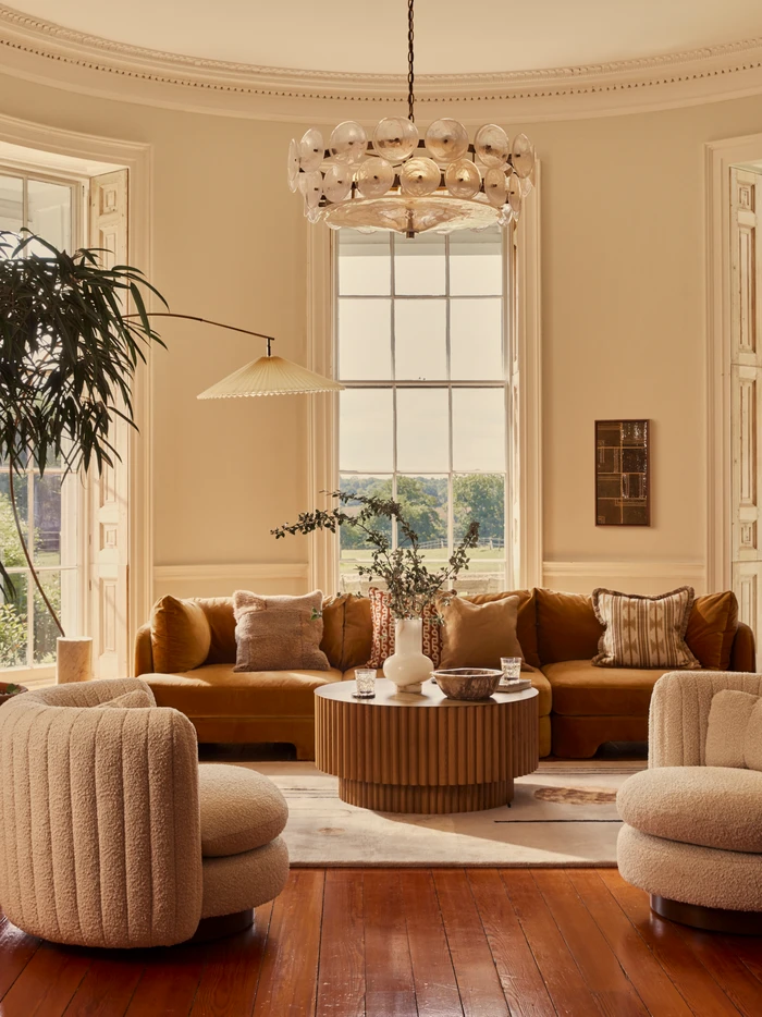 Spacious living room interior with a brown velvet sofa, two cream boucle armchairs, and a round wooden coffee table.