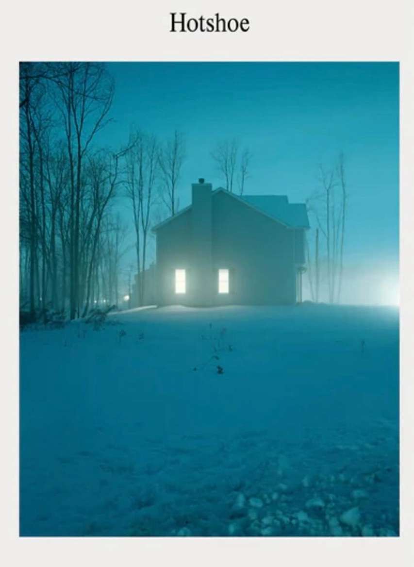 Two-story house with glowing windows at night, surrounded by snow and trees. Dramatic lighting and a cold color palette create a serene winter scene.